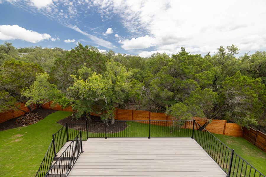 A spacious outdoor deck with wrought iron railing overlooks a fenced yard and dense natural landscaping.