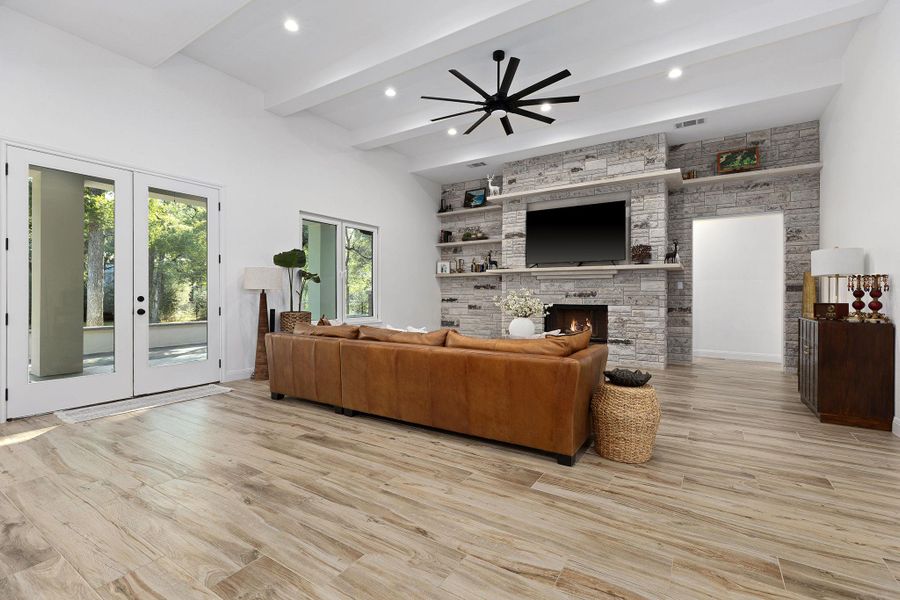 Living room with french doors, beam ceiling, light wood-style flooring, a stone fireplace, and recessed lighting Living room with french doors, beam ceiling, light wood-style flooring, a stone fireplace, and recessed lighting