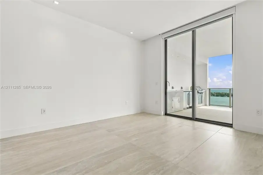 Large-format tile flooring, recessed ceiling lighting, and floor-to-ceiling sliding glass doors opening to a covered balcony with built-in cabinetry Large-format tile flooring, recessed ceiling lighting, and floor-to-ceiling sliding glass doors opening to a covered balcony with built-in cabinetry