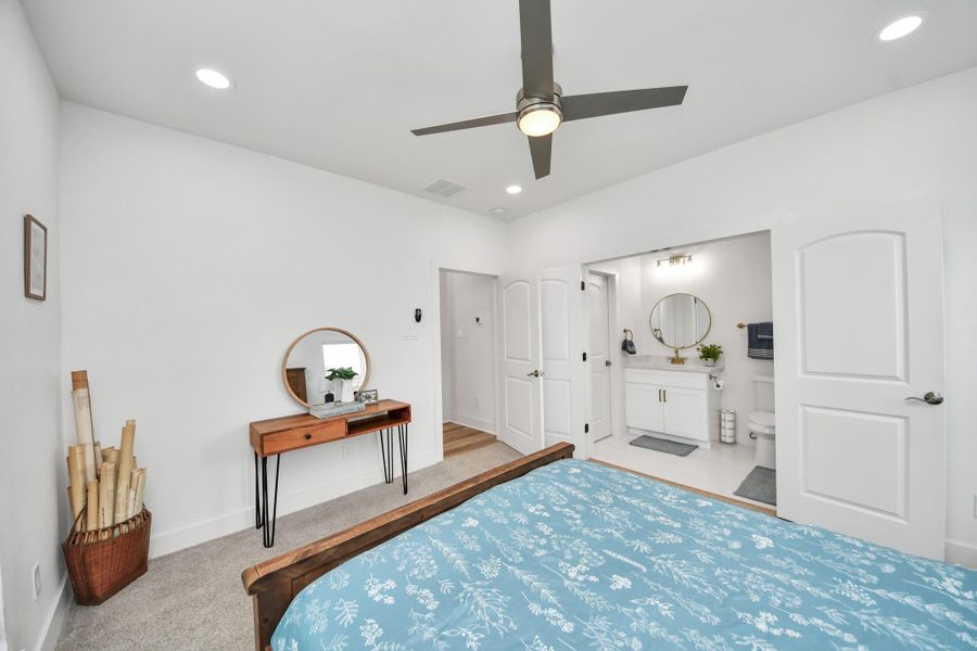 Spacious bedroom with modern ceiling fan, plush carpeting, and an en-suite bathroom featuring elegant fixtures and a sleek vanity. Spacious bedroom with modern ceiling fan, plush carpeting, and an en-suite bathroom featuring elegant fixtures and a sleek vanity.
