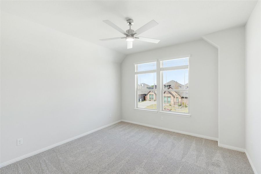 Empty bedroom with vaulted ceiling, ceiling fan, carpet flooring, and double windows overlooking neighborhood homes.