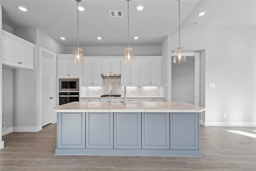 The kitchen anchors the space with light gray perimeter cabinetry, a bold blue island, a suite of modern stainless steel appliances, and sleek white quartz countertops that create an inviting hub perfect for casual dining or hosting.