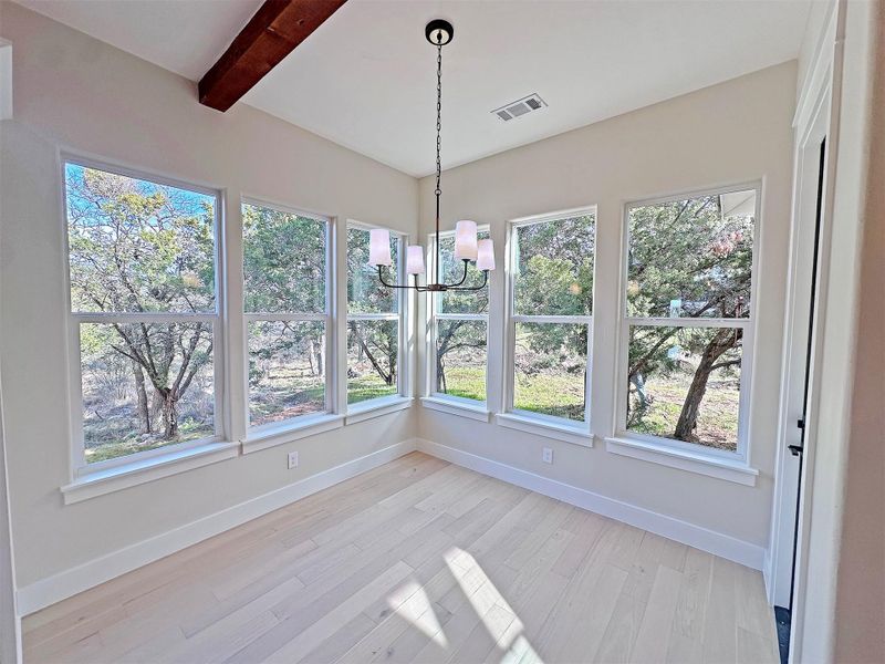 Sunny, window-filled dining area with a designer chandelier, beamed ceiling, and light oak hardwood floors