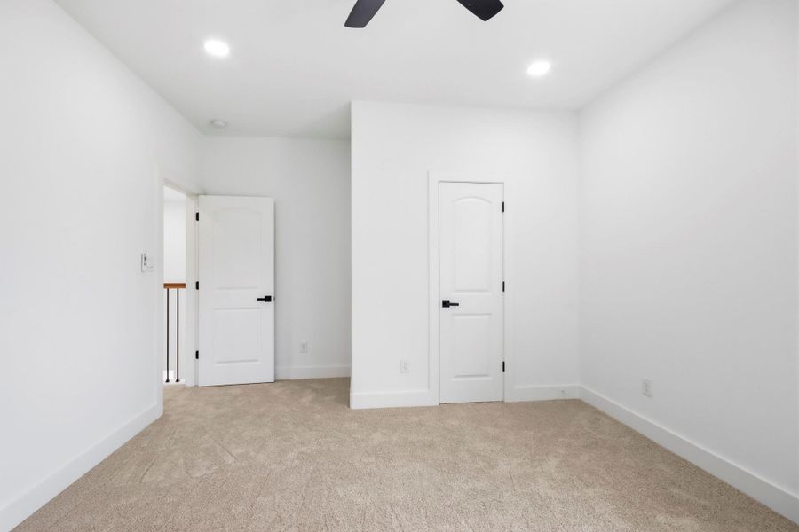 Bright and airy bedroom featuring soft carpet flooring, crisp white walls, and modern black hardware on doors for a sleek, contemporary look.