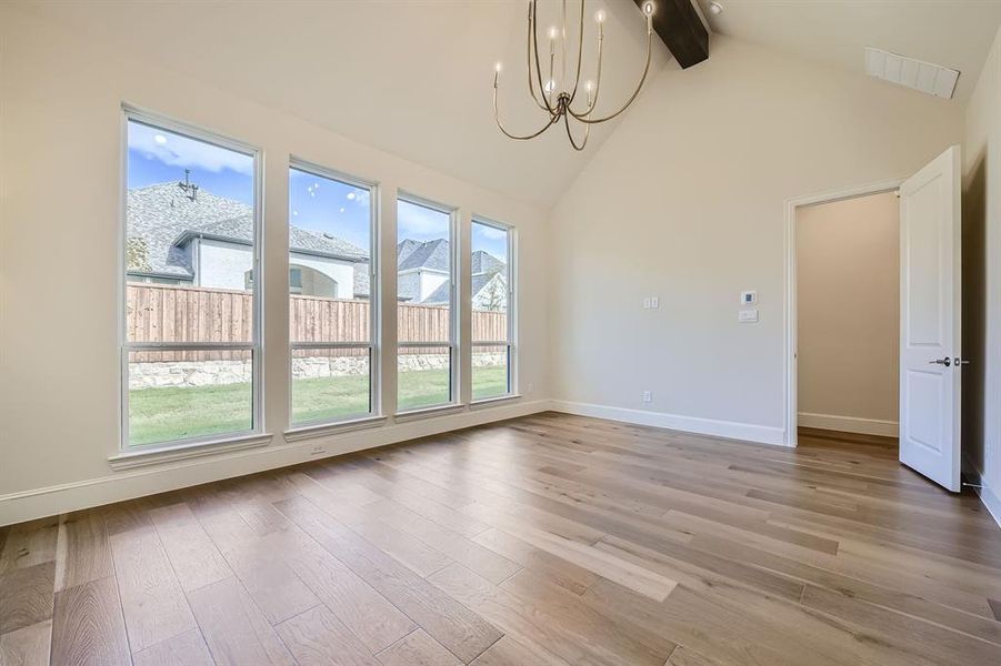 Primary bedroom with high vaulted ceiling, hardwood / wood-style flooring, beam ceiling, and an inviting chandelier