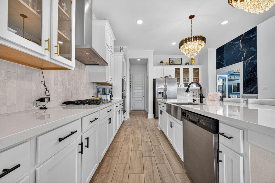 This kitchen features modern white cabinetry, stainless steel appliances, and elegant chandeliers. It has a spacious layout with a large island, sleek countertops, and wood-look flooring, creating a bright and inviting space. This kitchen features modern white cabinetry, stainless steel appliances, and elegant chandeliers. It has a spacious layout with a large island, sleek countertops, and wood-look flooring, creating a bright and inviting space.