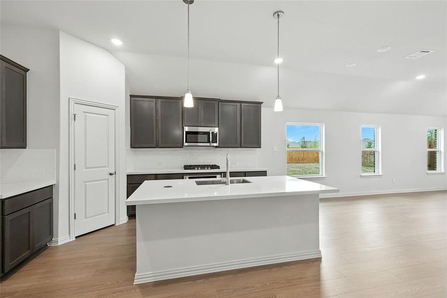 Kitchen with recessed lighting, light wood finished floors, light stone countertops, an island with sink, and dark brown cabinetry Kitchen with recessed lighting, light wood finished floors, light stone countertops, an island with sink, and dark brown cabinetry