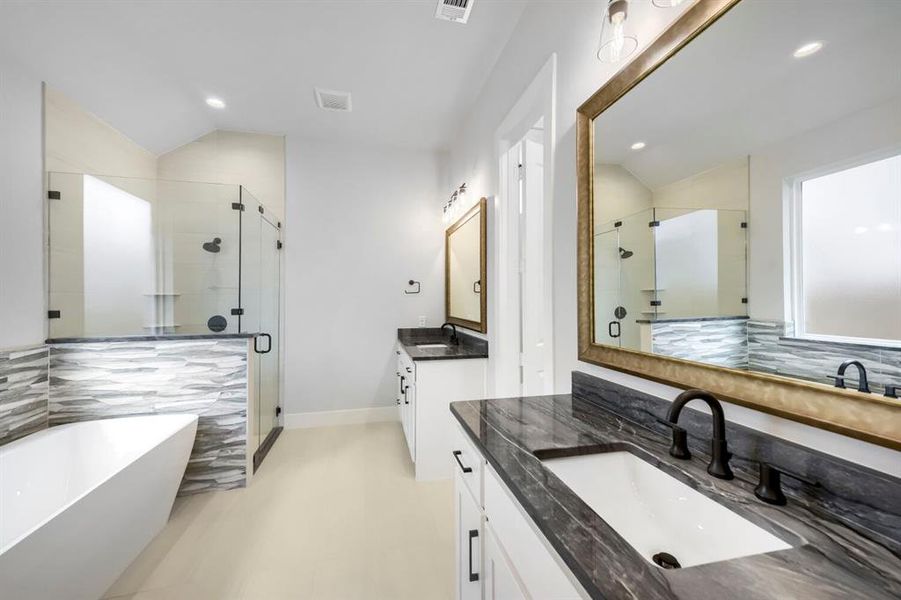 Freestanding soaking tub with a glass-enclosed shower, dual vanities featuring dark stone countertops, and matte black fixtures