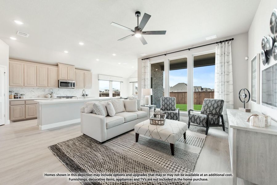 Open-concept living room and kitchen with light wood floors, ceiling fan, and large windows overlooking a backyard. Open-concept living room and kitchen with light wood floors, ceiling fan, and large windows overlooking a backyard.