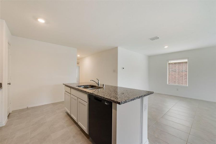 Kitchen featuring dark stone counters, white cabinets, sink, black dishwasher, and a kitchen island with sink