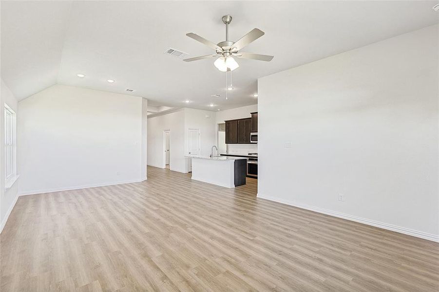 Unfurnished living room featuring ceiling fan, vaulted ceiling, sink, and light hardwood / wood-style flooring