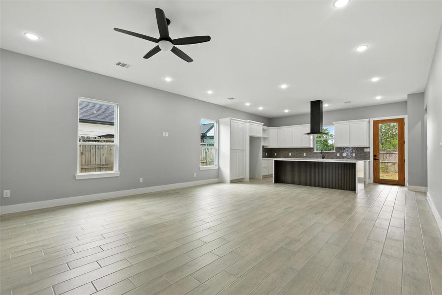 This spacious open-concept living area features modern flooring, a sleek ceiling fan, and ample natural light. The contemporary kitchen boasts white cabinetry, a stylish backsplash, and a large island with a range hood, perfect for entertaining.