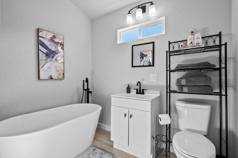 Full bath featuring a freestanding bath, vanity, a textured wall, and light wood-style floors.