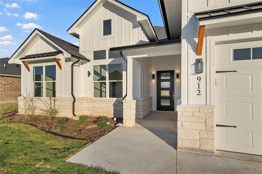 View of exterior entry featuring board and batten siding, a standing seam roof, stone siding, covered porch, and a metal roof