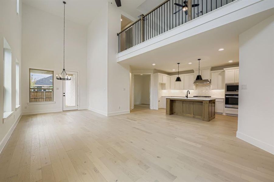 Unfurnished living room featuring a high ceiling, light wood finished floors, and a chandelier Unfurnished living room featuring a high ceiling, light wood finished floors, and a chandelier