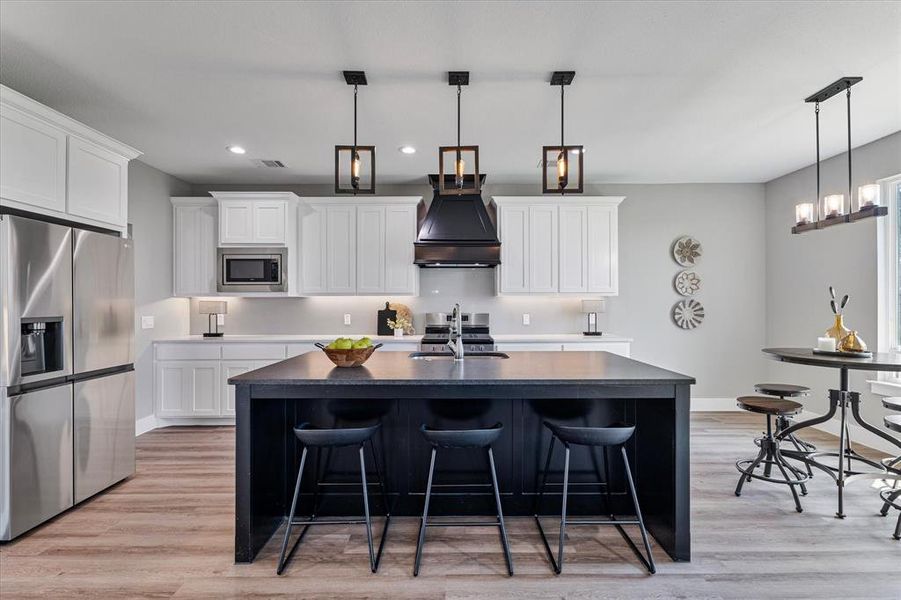 Kitchen with appliances with stainless steel finishes, light hardwood / wood-style floors, white cabinetry, a kitchen island with sink, and custom exhaust hood