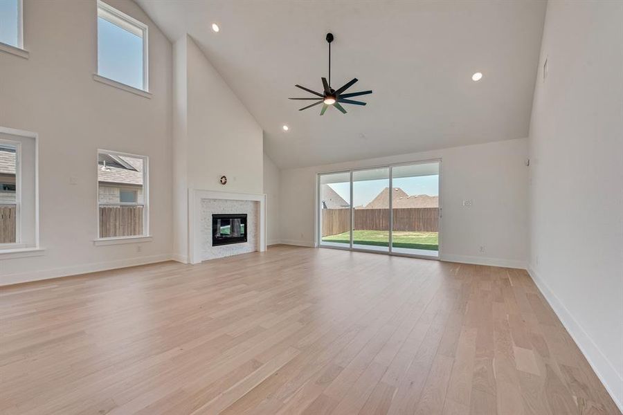 Unfurnished living room with recessed lighting, high vaulted ceiling, plenty of natural light, a glass covered fireplace, and light wood-type flooring Unfurnished living room with recessed lighting, high vaulted ceiling, plenty of natural light, a glass covered fireplace, and light wood-type flooring
