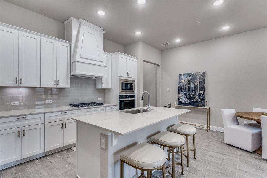 Kitchen featuring tasteful backsplash, a kitchen island with sink, white cabinets, premium range hood, and appliances with stainless steel finishes