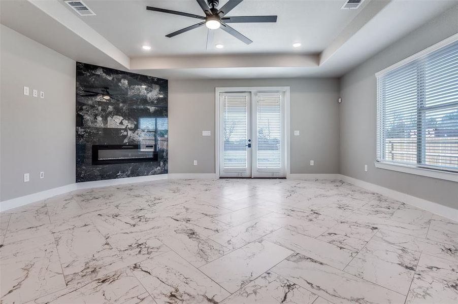 Unfurnished living room with a raised ceiling, french doors, a fireplace, ceiling fan, and recessed lighting