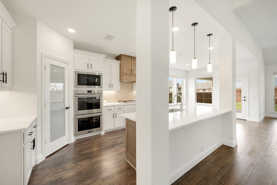 Kitchen with white cabinets, stainless steel double ovens, large island, pendant lights, and dark hardwood floors