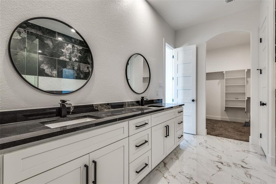 Bathroom with double vanity, a spacious closet, marble finish floor, and a sink