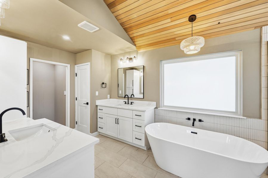 Bathroom featuring two vanities, a vaulted wood ceiling, a soaking tub, and light tile patterned floors