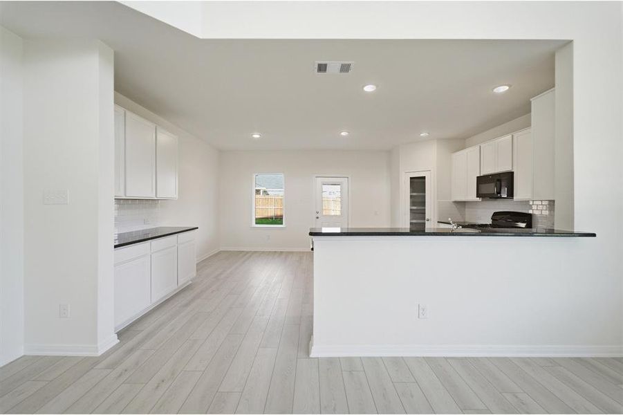 Open-concept kitchen featuring white cabinetry, dark countertops, a tile backsplash, recessed lighting, and wood-finish flooring