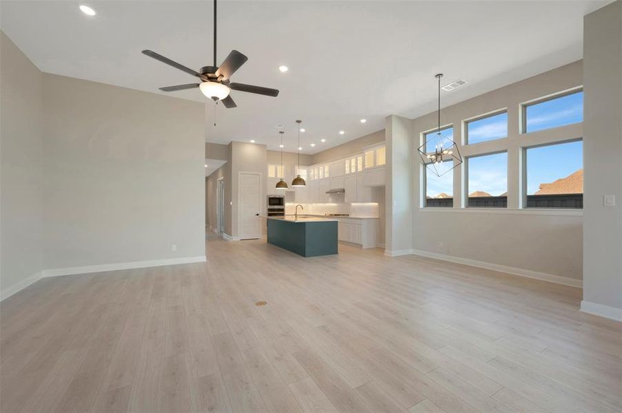 Unfurnished living room featuring hanging lights, ceiling fan, and light wood finished floors Unfurnished living room featuring hanging lights, ceiling fan, and light wood finished floors