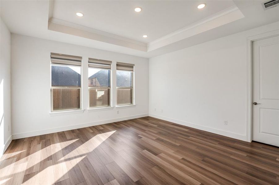 Primary bedroom featuring dark wood-style floors, a raised ceiling, recessed lighting, and ornamental molding Primary bedroom featuring dark wood-style floors, a raised ceiling, recessed lighting, and ornamental molding