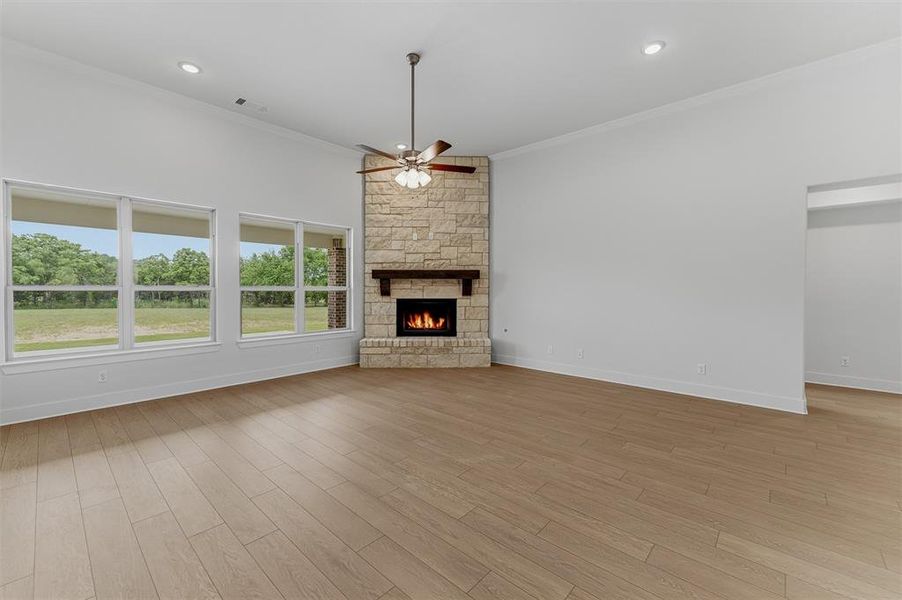 Open living space featuring wood-finish flooring, a corner stone fireplace with wood mantel, a ceiling fan, recessed lighting, and multiple windows Open living space featuring wood-finish flooring, a corner stone fireplace with wood mantel, a ceiling fan, recessed lighting, and multiple windows