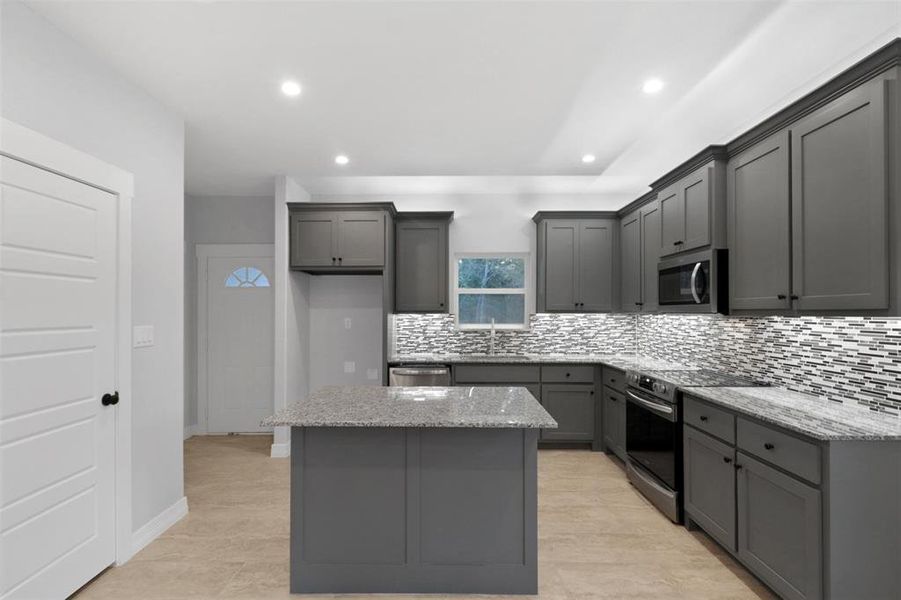 Kitchen with light stone counters, gray cabinets, a center island, appliances with stainless steel finishes, and backsplash Kitchen with light stone counters, gray cabinets, a center island, appliances with stainless steel finishes, and backsplash