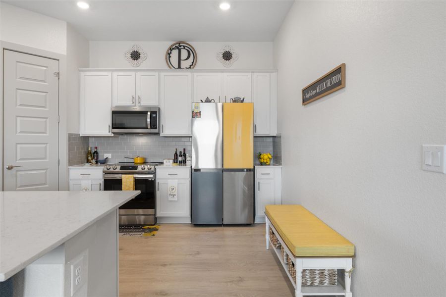 Kitchen with stainless steel appliances, white cabinets, backsplash, light stone countertops, and light wood-style floors Kitchen with stainless steel appliances, white cabinets, backsplash, light stone countertops, and light wood-style floors