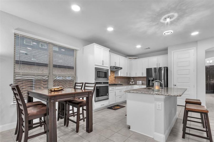 Kitchen with a center island with sink, white cabinets, appliances with stainless steel finishes, light stone counters, and under cabinet range hood