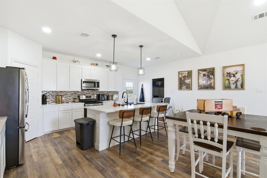 Kitchen with a kitchen bar, stainless steel appliances, an island with sink, tasteful backsplash, and dark wood-type flooring Kitchen with a kitchen bar, stainless steel appliances, an island with sink, tasteful backsplash, and dark wood-type flooring