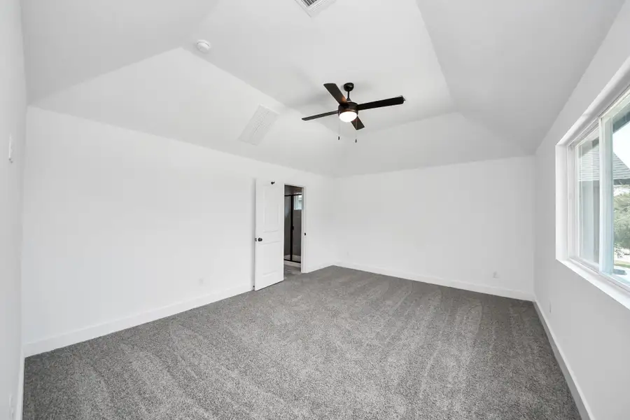 Primary Bedroom – Spacious and bright primary suite with plush carpeting, modern ceiling fan, large windows, and plenty of natural light.