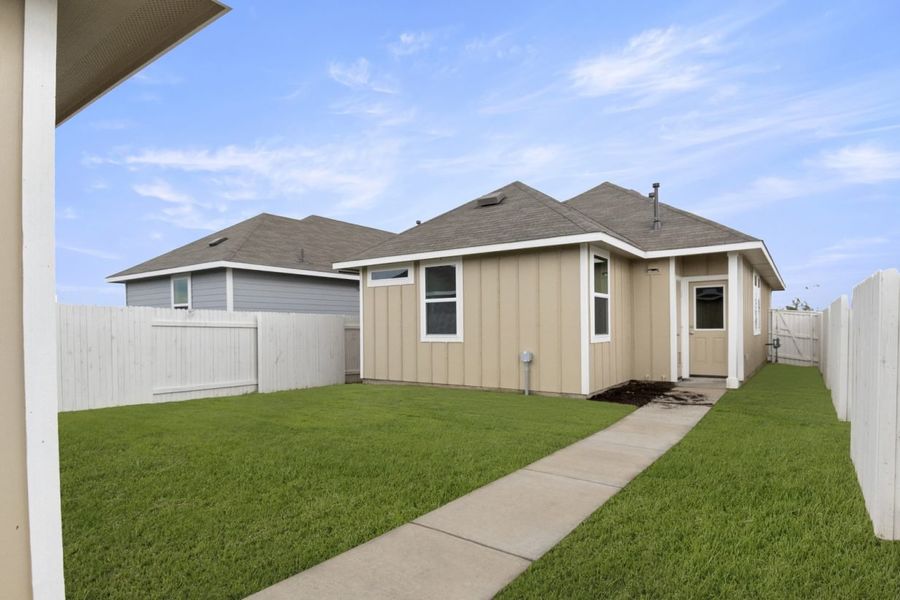 Image of an exterior tan one story home with a backyard and fence with green grass and a blue sky
