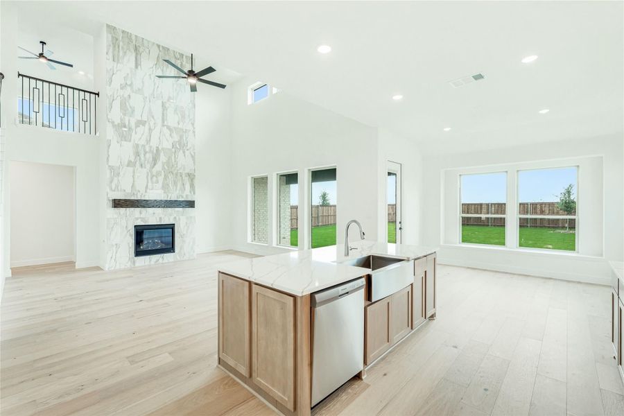 Open-concept kitchen and living area with large island, stone fireplace, high ceilings, and light wood floors