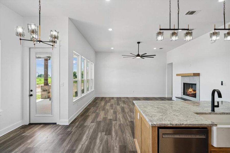 Kitchen with dishwasher, dark wood-style flooring, a tiled fireplace, a chandelier, and recessed lighting