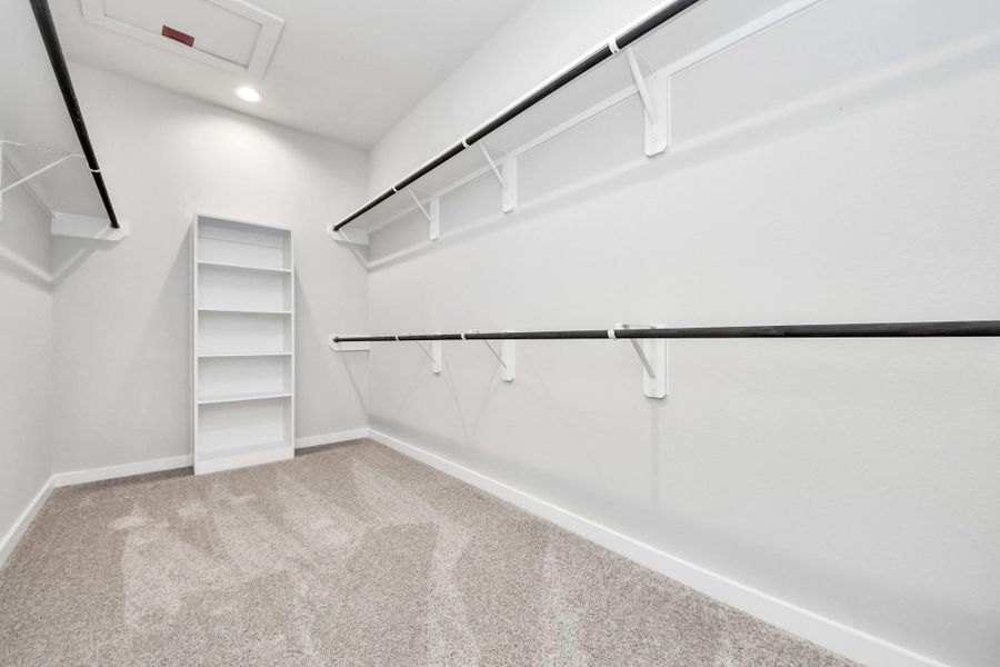 Walk-in closet that epitomizes luxury and practicality. This generously sized space features built-in shelving, offering abundant room for impeccable organization. High ceilings and recessed lighting create a bright and welcoming ambiance. Sample photo of completed home with similar floor plan. Actual colors and selections may vary.
