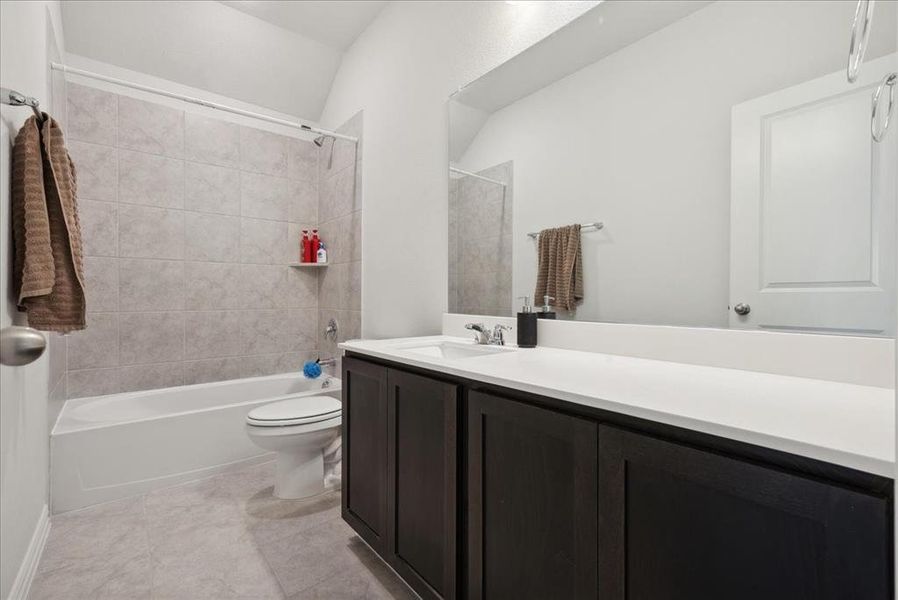 Full bathroom with tile patterned flooring, vanity, tiled shower / bath combo, and toilet