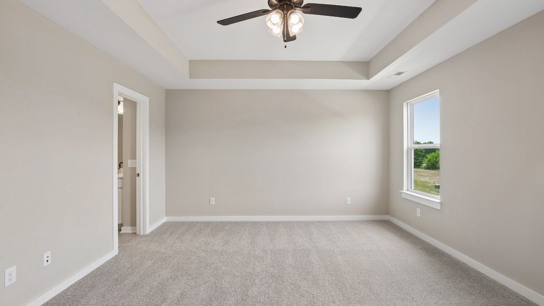 Bedroom with tray ceiling, windows, and en-suite primary bathroom