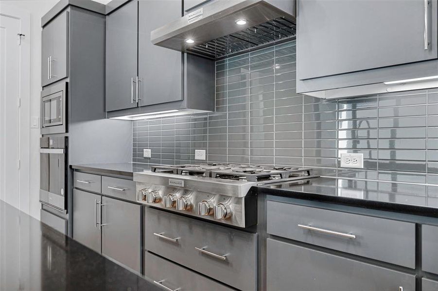 Kitchen with appliances with stainless steel finishes, ventilation hood, backsplash, and gray cabinetry