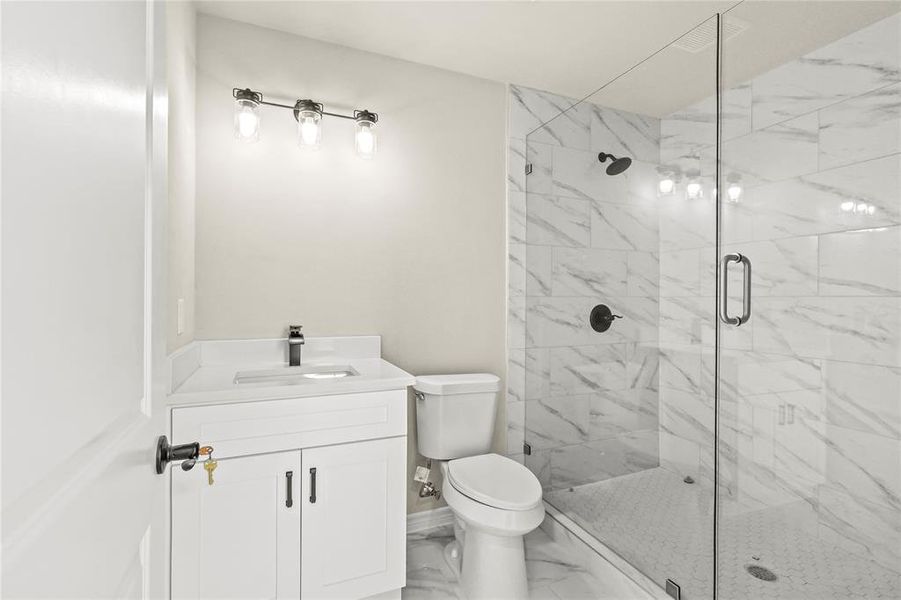 Bathroom featuring a shower with door, vanity, and toilet