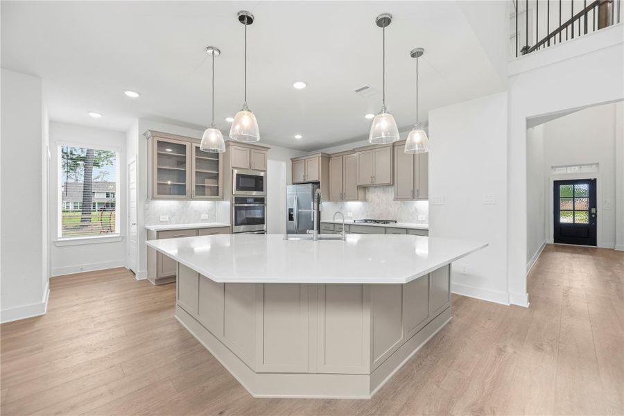Gourmet kitchen features a huge island, luxurious countertops, under cabinet lighting, stainless steel appliances, double ovens, gas cooktop and glass front cabinets.