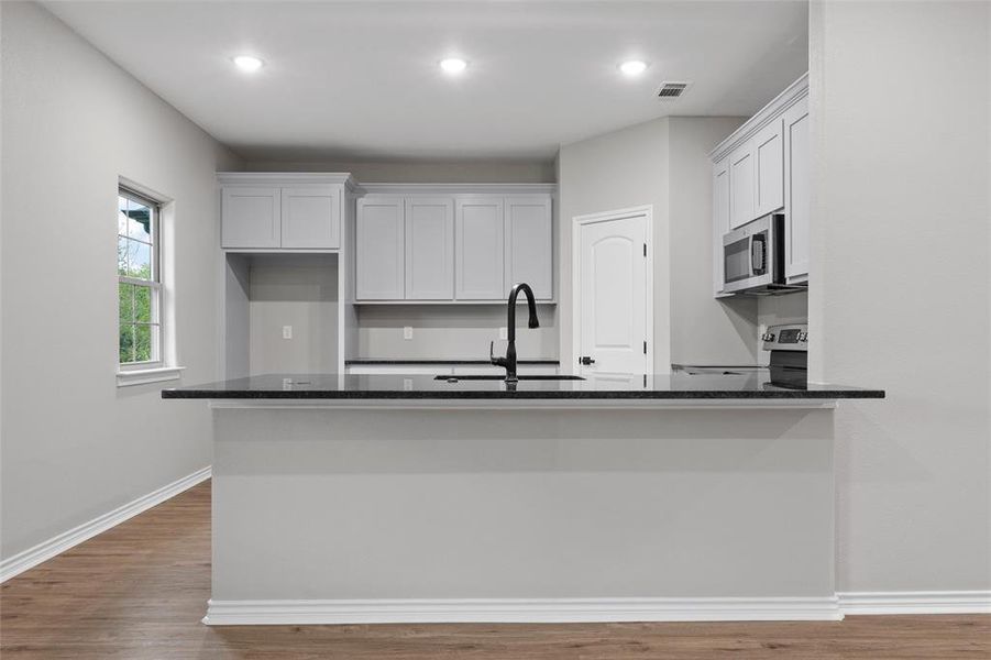 Kitchen with dark stone counters, dark wood-type flooring, white cabinets, a peninsula, and recessed lighting
