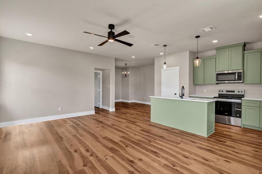 Kitchen with green cabinetry, stainless steel appliances, a kitchen island with sink, a chandelier, and recessed lighting
