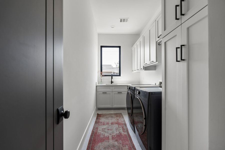 The spacious utility room is located upstairs with the primary bedroom and 2 secondary beds and features upper and lower cabinetry, a countertop for folding, utility sink with black plumbing fixtures, a hanging rod, light tile flooring, and a window for added natural light.