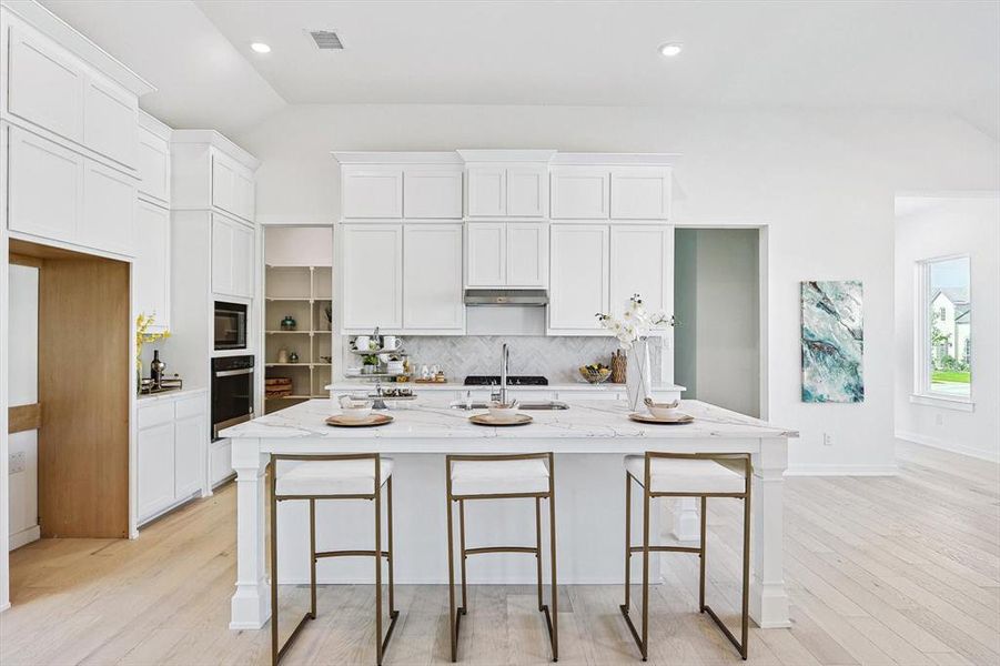 Kitchen with vaulted ceiling, a kitchen island with sink, oven, and light stone countertops