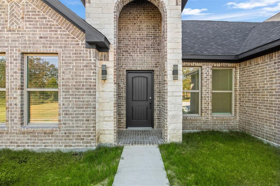View of exterior entry with brick siding and a shingled roof