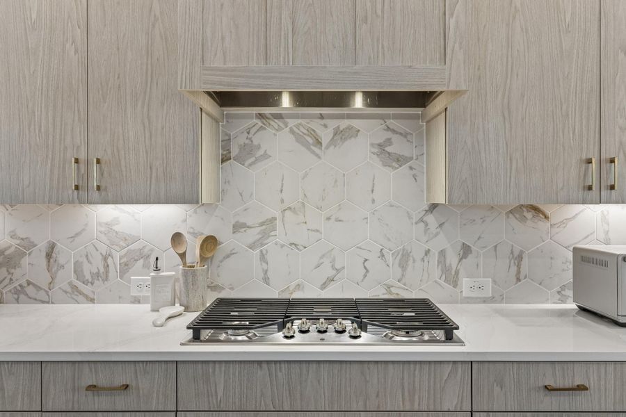 A sophisticated gas cooktop pairs beautifully with elegant stone counters and a geometric backsplash.